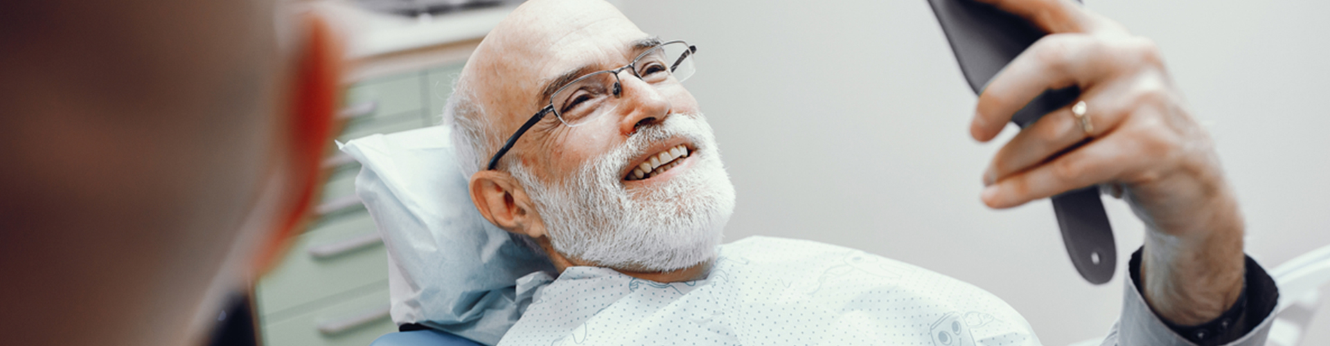 man admiring smile in hand mirror in dental chair.
