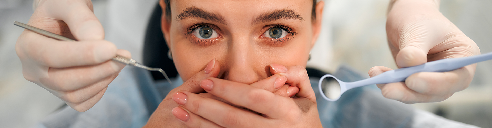 gloved hands holding dental tools next to woman covering her mouth.