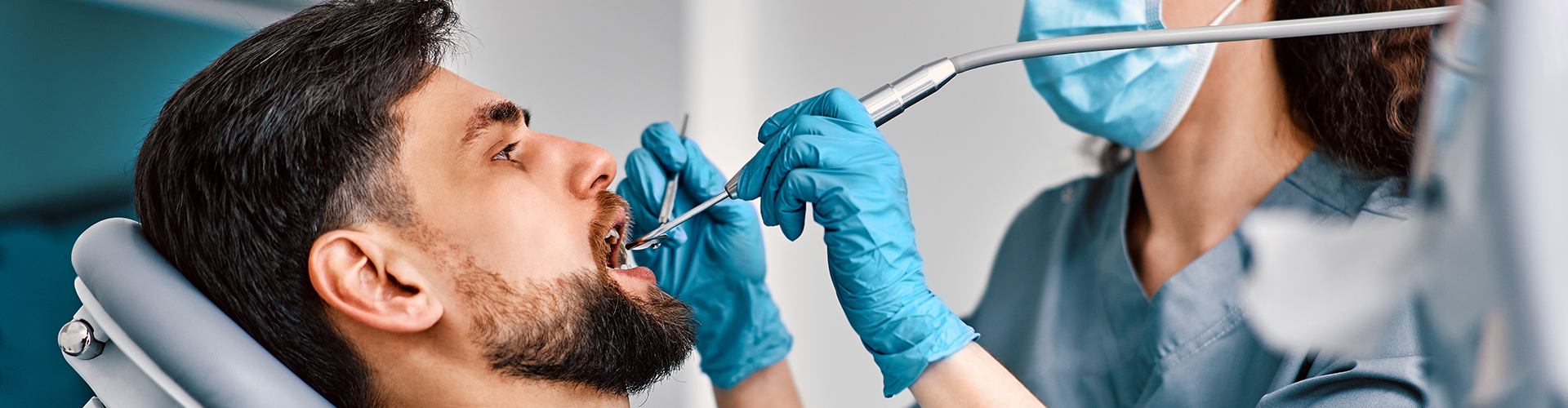 dentist using dental tools in man's mouth in dental office.