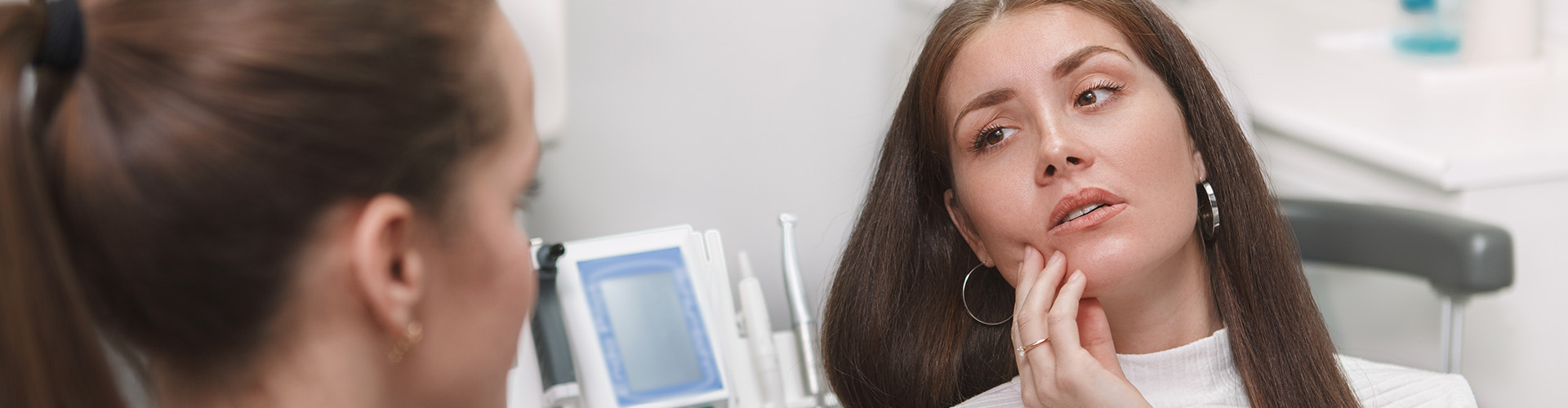 woman in dental office holding jaw in pain looking at dentist.