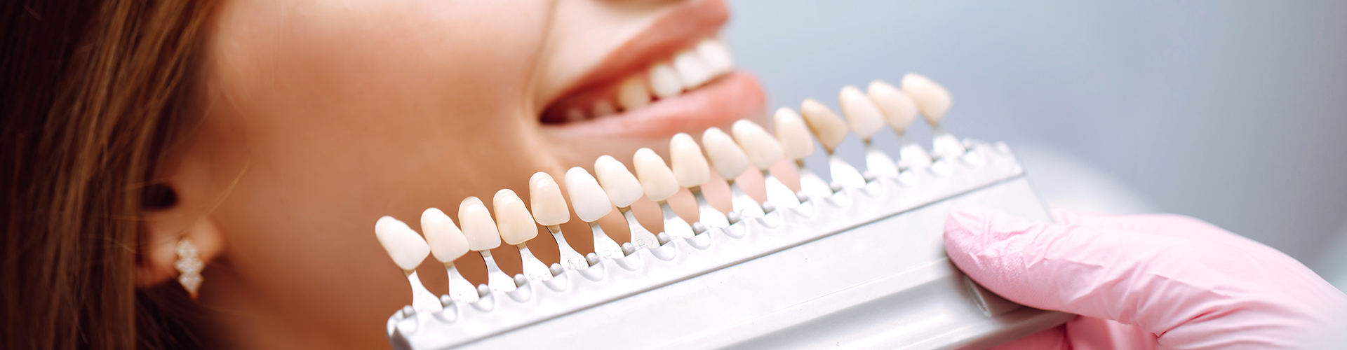 gloved hands holding color-matching tool against woman's teeth.