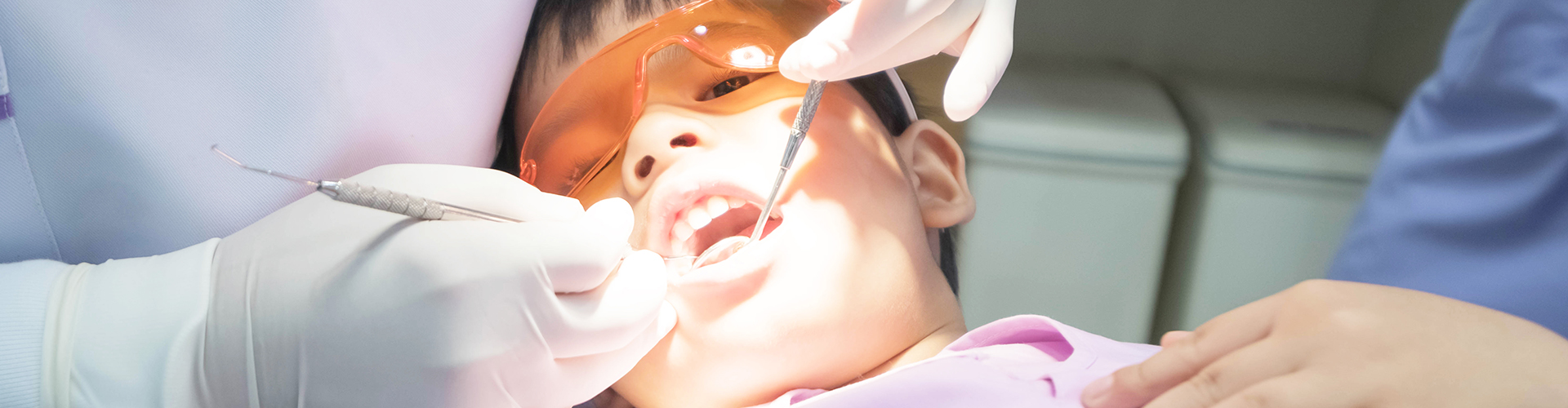gloved hands using dental tools in child's mouth.