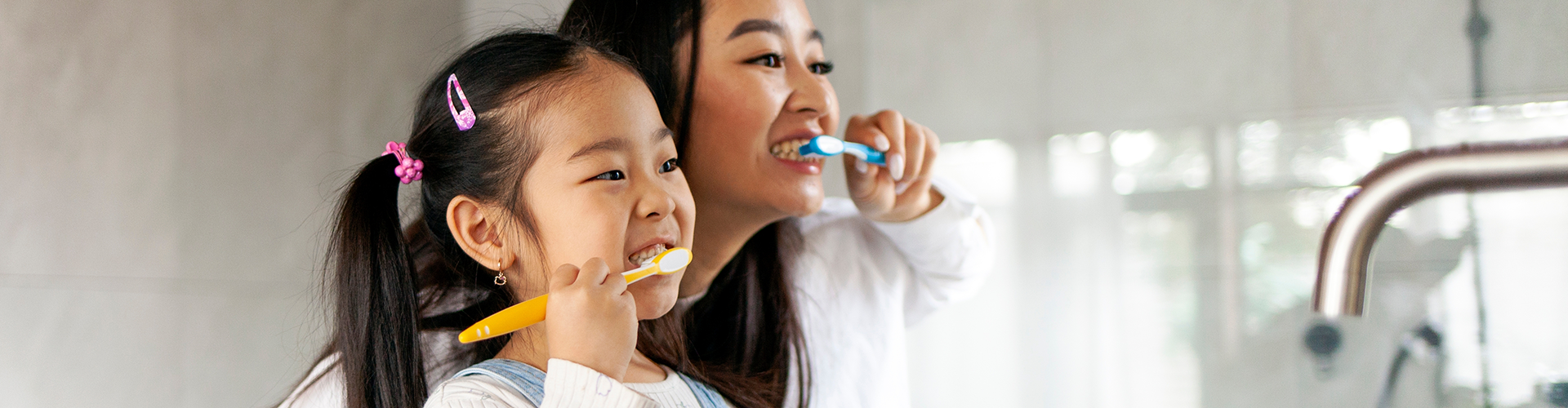 woman and young girl brushing teeth together.