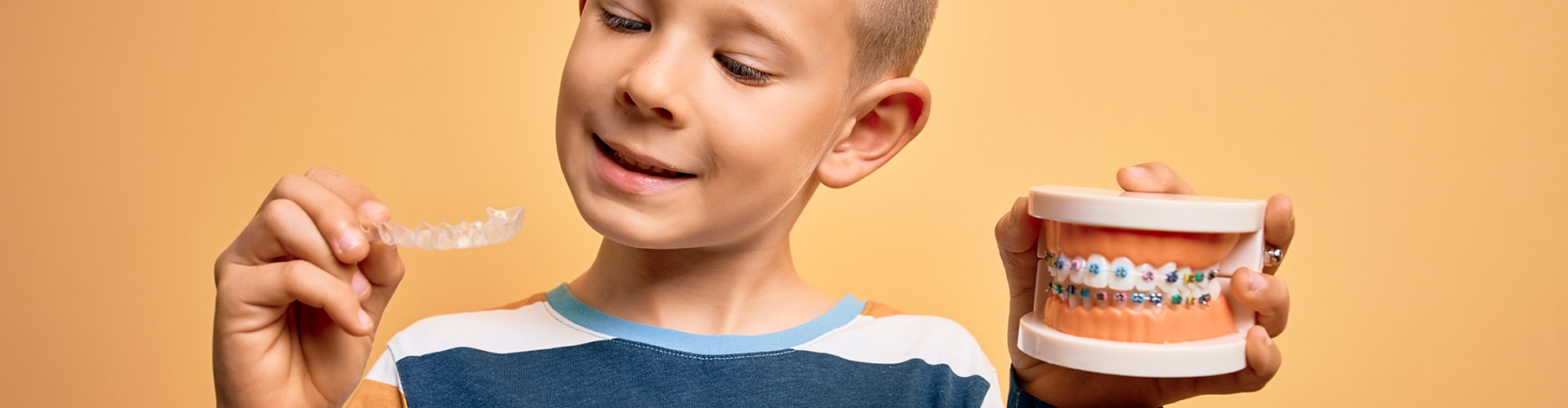 child holding clear aligners in one hand and a mouth model with braces in the other.