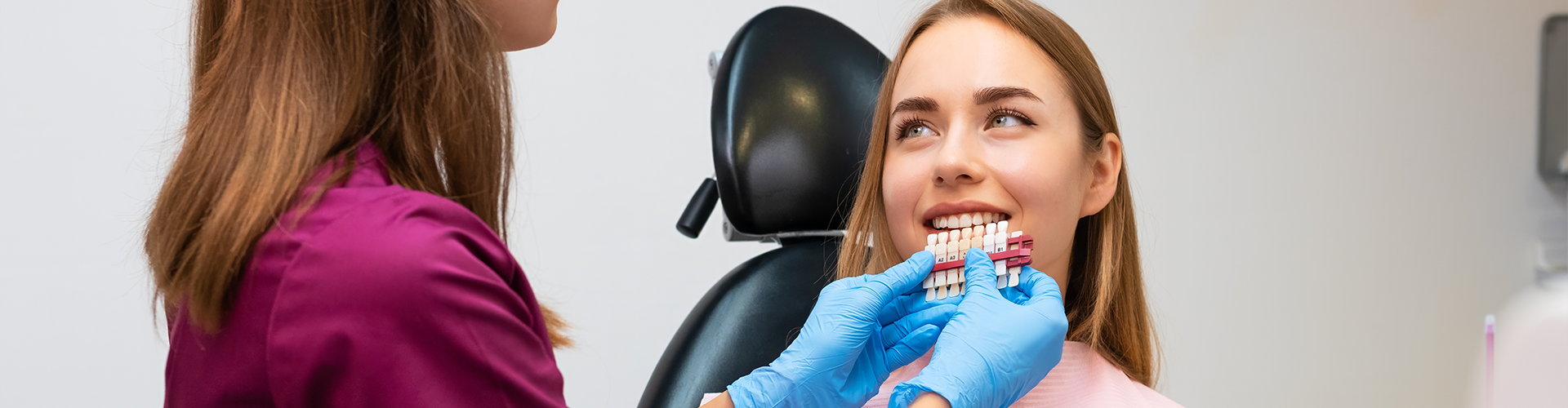 dentist holding shade-matching tool against woman's smile.