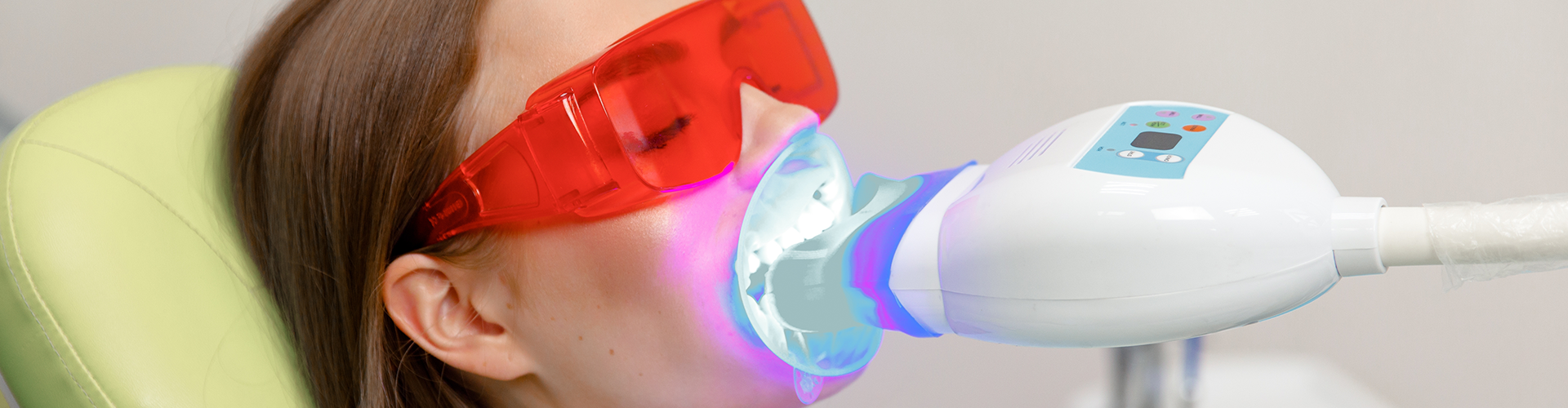 led light shining on teeth of woman wearing orange glasses.