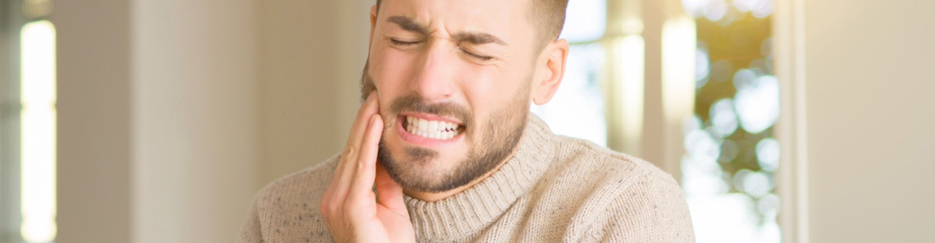 Man holding the left side of his face clenching his teeth.