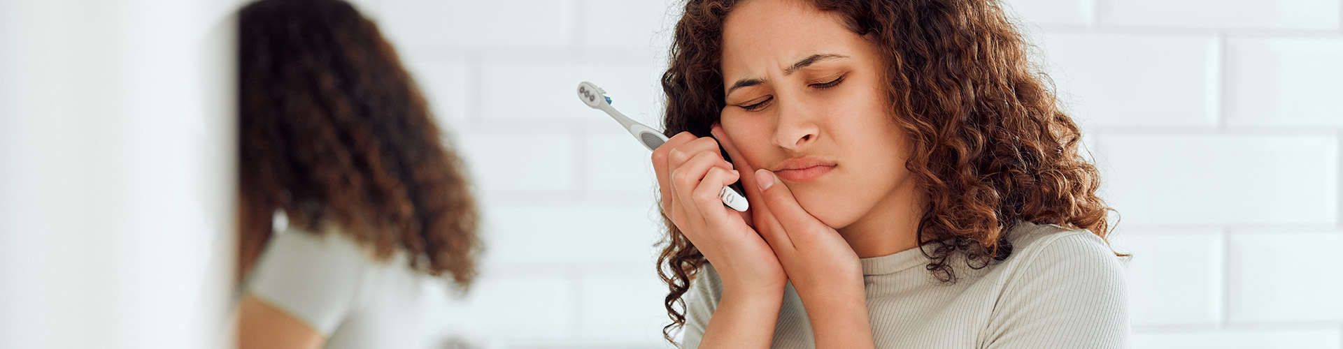 woman with toothbrush holding her cheek in pain.