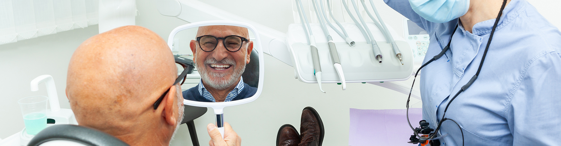 man smiling into hand mirror while dentist watches.