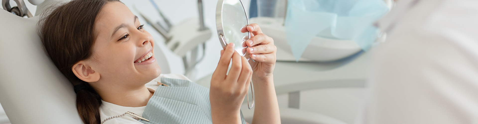 child admiring her smile in hand mirror.